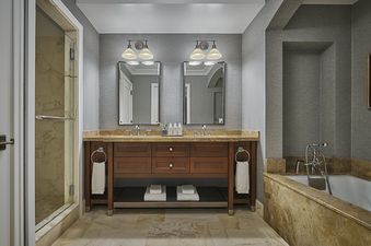 The primary bathroom features a double vanity with two sinks, two mirrors, a walk-in shower with a glass door, and a bathtub.