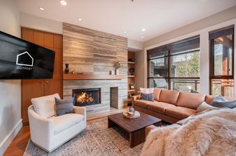 Cozy living room with a stone fireplace, leather sofa, and forest views at Ravencrest 204.