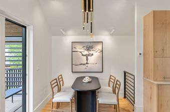 A modern dining area at Depot House featuring a black oval table with white sculptural decor, four wooden chairs, and a striking black-and-white ski photograph on the wall, under a gold and black cylindrical chandelier.