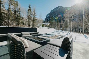 A modern outdoor living space with a fire pit and hot tub overlooking a snowy mountainside.