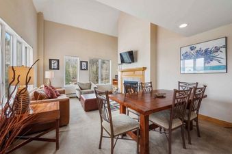 A spacious and inviting open-concept living and dining area featuring comfortable seating, a large dining table, a fireplace, and large windows with outdoor views.