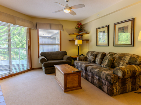 A spacious and inviting living room at Aspens on Blackcomb Unit 438, featuring comfortable seating, a coffee table, and large windows with blinds.