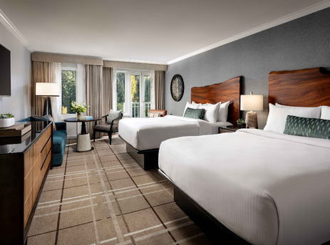 A spacious Fairmont Chateau Queen and Queen Room with two queen beds, a sitting area, a dresser with a wall-mounted TV, and a large window offering an outdoor view.