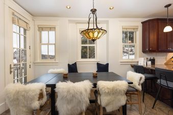 A dining table with chairs, nestled between windows that offer a glimpse of the snowy outdoors, creating a cozy and inviting atmosphere.