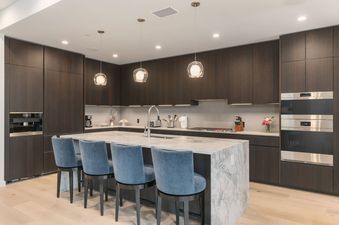 Modern gourmet kitchen with a large marble island, blue barstools, and dark wood cabinetry at Sky View Jackson Hole.