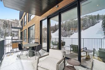 A private balcony at Founders Place 2403 overlooks a snowy mountain landscape, featuring modern outdoor furniture and large sliding glass doors.