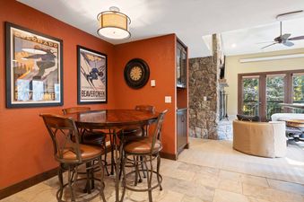 A cozy dining area at The Charter C2105 features a round dark wood table, four bar stools with leather seats, and ski-themed wall decor.