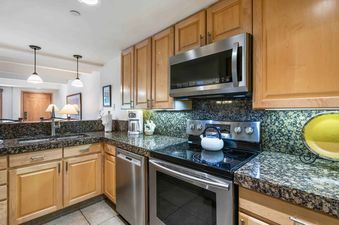 A modern kitchen with stainless steel appliances, wood cabinets, and granite countertops.