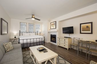 A comfortable studio unit at Fraser Crossing Studio 3518, featuring a bed, a sofa, a dining table, a television, and a fireplace.