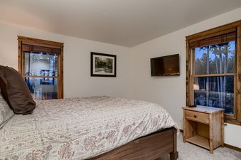 A cozy bedroom at Lodge at Ski Hill with a bed featuring patterned linens, a wall-mounted TV, and two large windows offering a view of the outdoors.