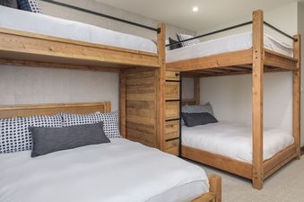 A bedroom with a bunk bed and a twin bed with white bedding and black and white patterned pillows.