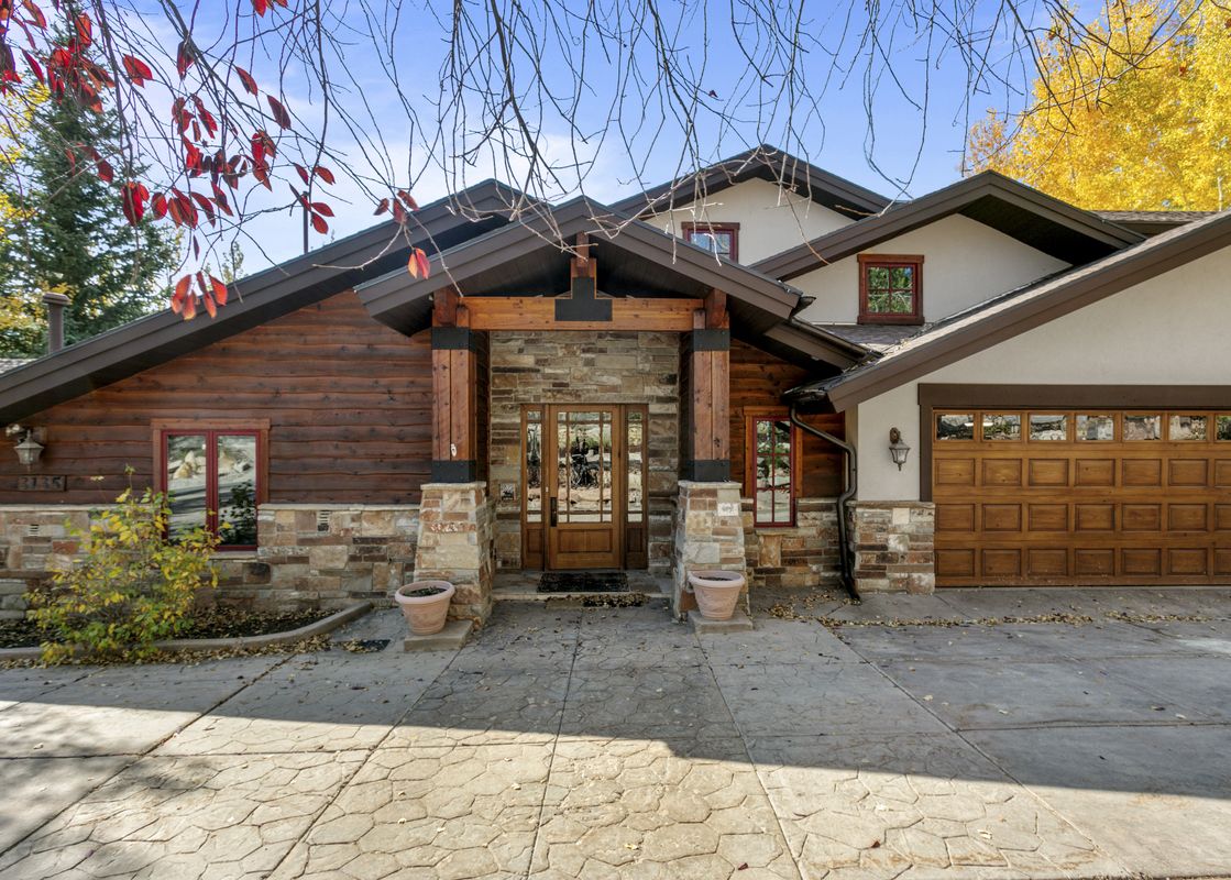 A rustic home with stone accents and a wooden front door, a wood-paneled garage door and a patterned concrete driveway.