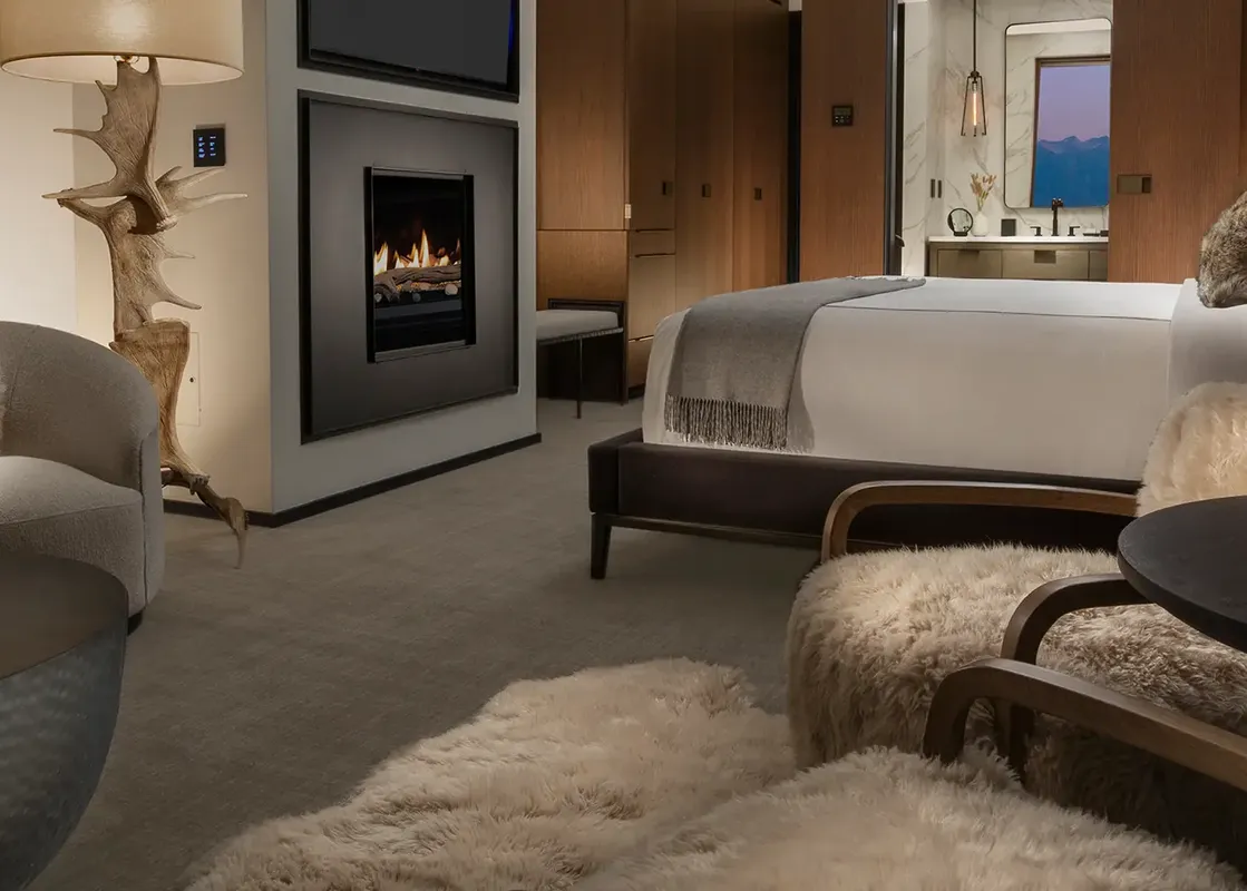 A luxurious hotel suite featuring a fireplace, a king-sized bed, a cozy seating area, and an en-suite bathroom visible in the background.
