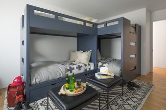 A modern bunk room at Jackson View with L-shaped blue-gray bunk beds, two ottomans, a patterned rug, and a light wooden floor.