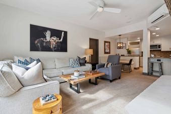 A comfortable and well-appointed living area in The Charter F2305 with a large L-shaped sofa, a wooden coffee table, and an artwork featuring a moose, leading into a dining area and kitchen.