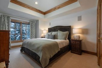 The primary bedroom features a large, comfortable bed with an upholstered headboard, flanked by wooden nightstands with lamps, and a large window offering a snowy winter view.