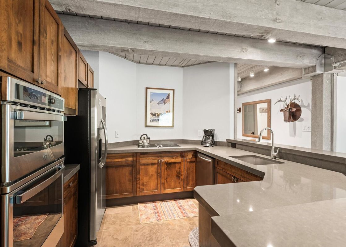 A modern kitchen in Enclave 211 with wooden cabinets, stainless steel appliances, gray countertops, and a ski poster on the wall.