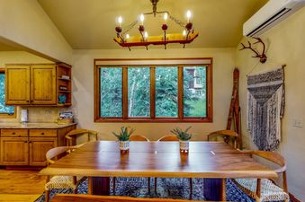 Dining table under a rustic chandelier with views of lush trees outside.