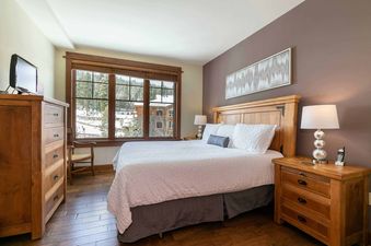 A bedroom with a king-sized bed, a wooden dresser, and a window overlooking a snowy mountain scene.