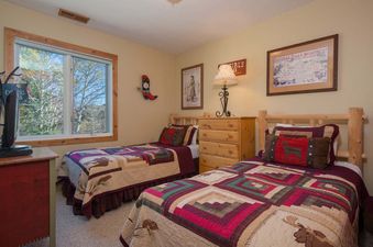 A rustic twin bedroom at Whiteridge B3 featuring two twin beds with colourful patchwork quilts and a window overlooking green trees.