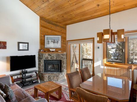 The Pines Condominiums A304's living and dining room with a stone fireplace and views of a snowy landscape.