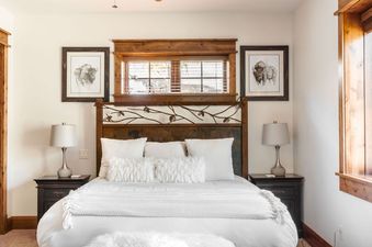A luxurious king bedroom at Antler Ridge 316 with a rustic wooden headboard, white linens, and bison artwork on the walls.