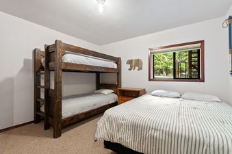 A children's bedroom featuring a wooden bunk bed, a full-sized bed, and a window with an outdoor view.