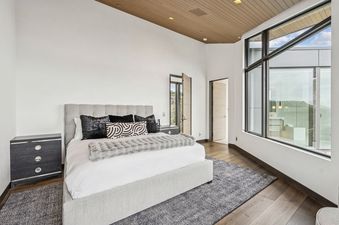 A modern master bedroom at Mountainhead featuring a large grey upholstered bed, white walls, dark wood floors, and expansive windows offering mountain views.