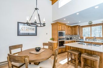 A modern kitchen and dining area with wooden cabinets, a large window, and a round dining table.