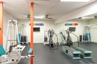 A well-equipped gym at TRISTANT 115 with weight machines, cardio equipment, and mirrors.