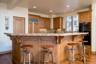 A kitchen island with bar seating and a granite countertop in a luxury home with a wood-paneled kitchen.