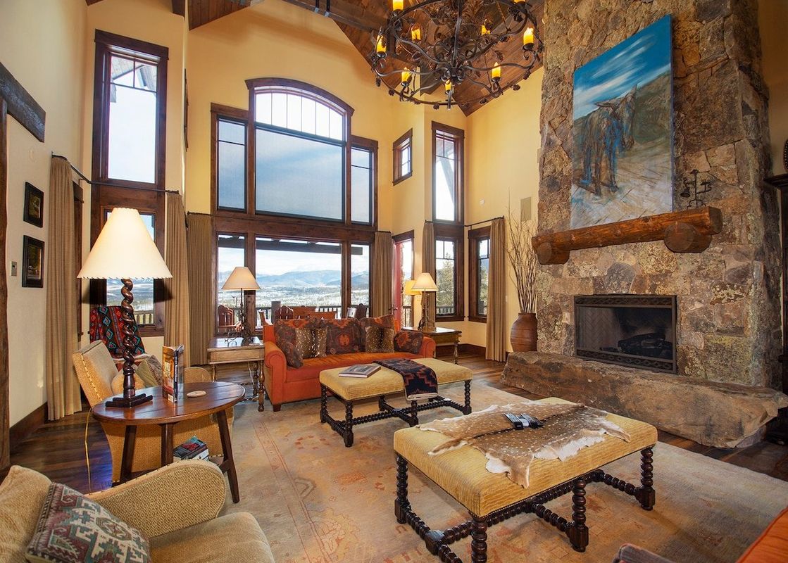The living area at 492 Golf Course Circle boasts a grand stone fireplace, a large chandelier, and expansive windows.