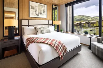 A cozy bedroom with a king-sized bed, plaid throw blanket, and a large window overlooking a scenic mountain view.