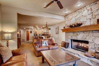 The inviting living area of Town Pointe B203 features a leather sofa, a decorative coffee table, and a stone fireplace, with a peek into the kitchen.