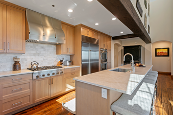 The kitchen of Grand Lodge Five Bedroom Penthouse 406 features stainless steel appliances, a large island with seating, and a beautiful wood floor.