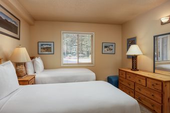 The second bedroom at Vantage Point 102 with two full-sized beds, a nightstand, a dresser with a mirror, and framed artwork on the walls.