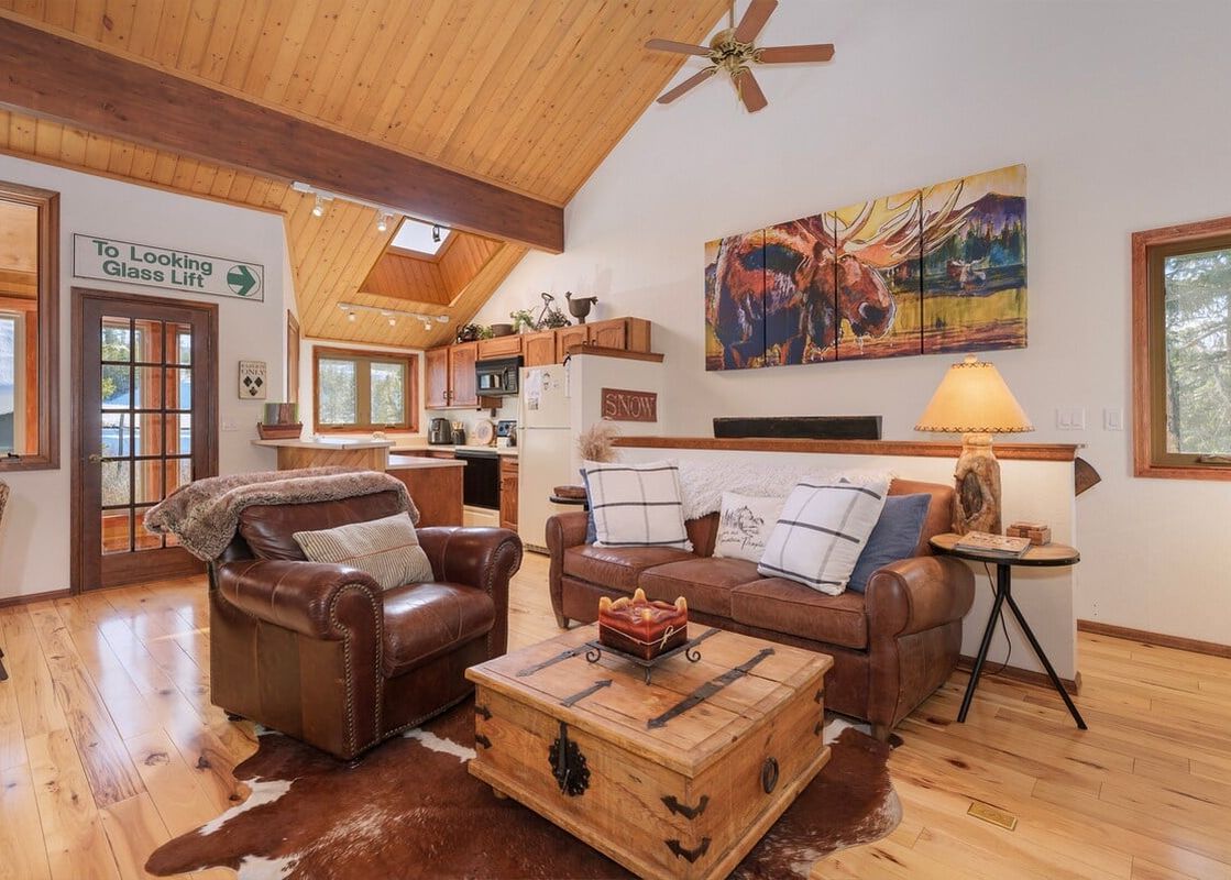 The living area of Kings Crossing townhome 13 features vaulted wood ceilings, a comfortable brown leather sofa and armchair, and a rustic wooden coffee table.