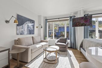 A modern living room at Galleria 307 with a beige sofa, glass coffee table, and a large window looking out onto a scenic view.