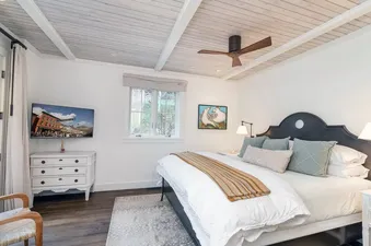 A cozy bedroom at East End Estate featuring a king-sized bed, a wall-mounted TV, and a large window.