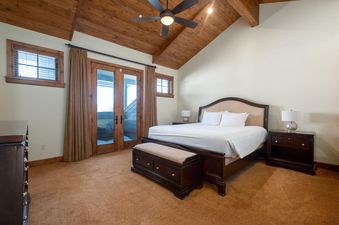 The bedroom at Snowtop Manor features a vaulted wooden ceiling, a large bed with dark wood furnishings, and French doors leading to an outdoor space.