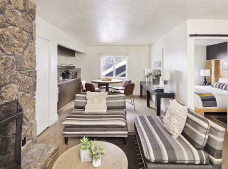 Living room of the Gravity Haus JH One Bedroom King Suite, showcasing a fireplace, striped seating, and an adjacent bedroom.