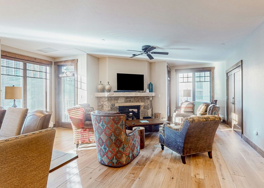 A living room with a stone fireplace, a large flat-screen TV, a couch, and a set of comfortable armchairs.
