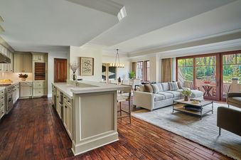 An expansive open-concept living space features a modern kitchen, a spacious living room, and a dining area, all seamlessly connected and leading to a large balcony with lush green views.