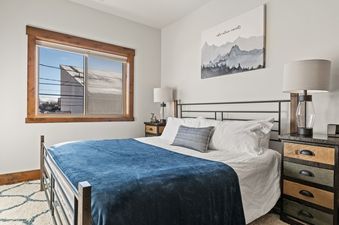 A cozy bedroom at Baker Loft 201 featuring a comfortable bed with a blue throw, two nightstands with lamps, and a window with a view.