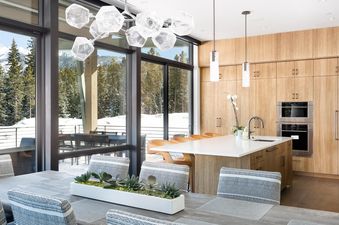 The dining area in Moonlight Basin 8C Speedwell features a large table and chairs, with a view of the snowy mountains outside the window.