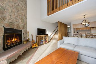The Meadow Ridge 31 living area features a stone fireplace, a flat-screen TV on a wooden cabinet, and a comfortable light gray sofa.