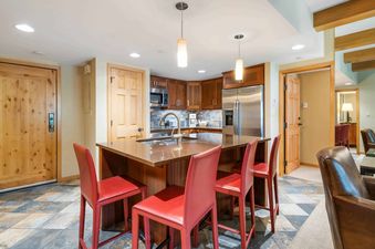 A kitchen with a stainless steel refrigerator, a double sink, and a kitchen island with red bar stools.