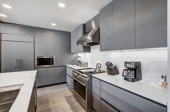 The kitchen at Snow Cloud Lodge 506 features sleek grey cabinetry, white marble countertops, and stainless steel appliances, including an oven, microwave, and refrigerator.