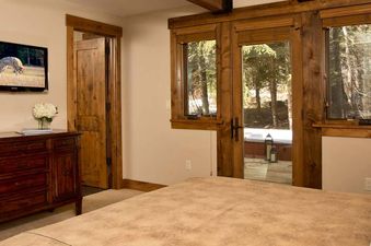 Primary bedroom with a king bed, wood dresser, wall-mounted TV, and glass doors leading to a patio at Blue Moose Lodge.