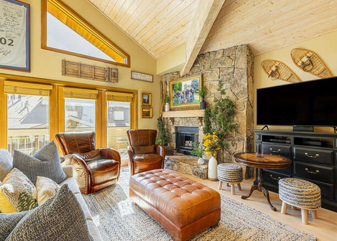 A spacious living area in Royal Plaza 403 featuring a prominent stone fireplace, comfortable brown leather seating, and large windows with exterior views.